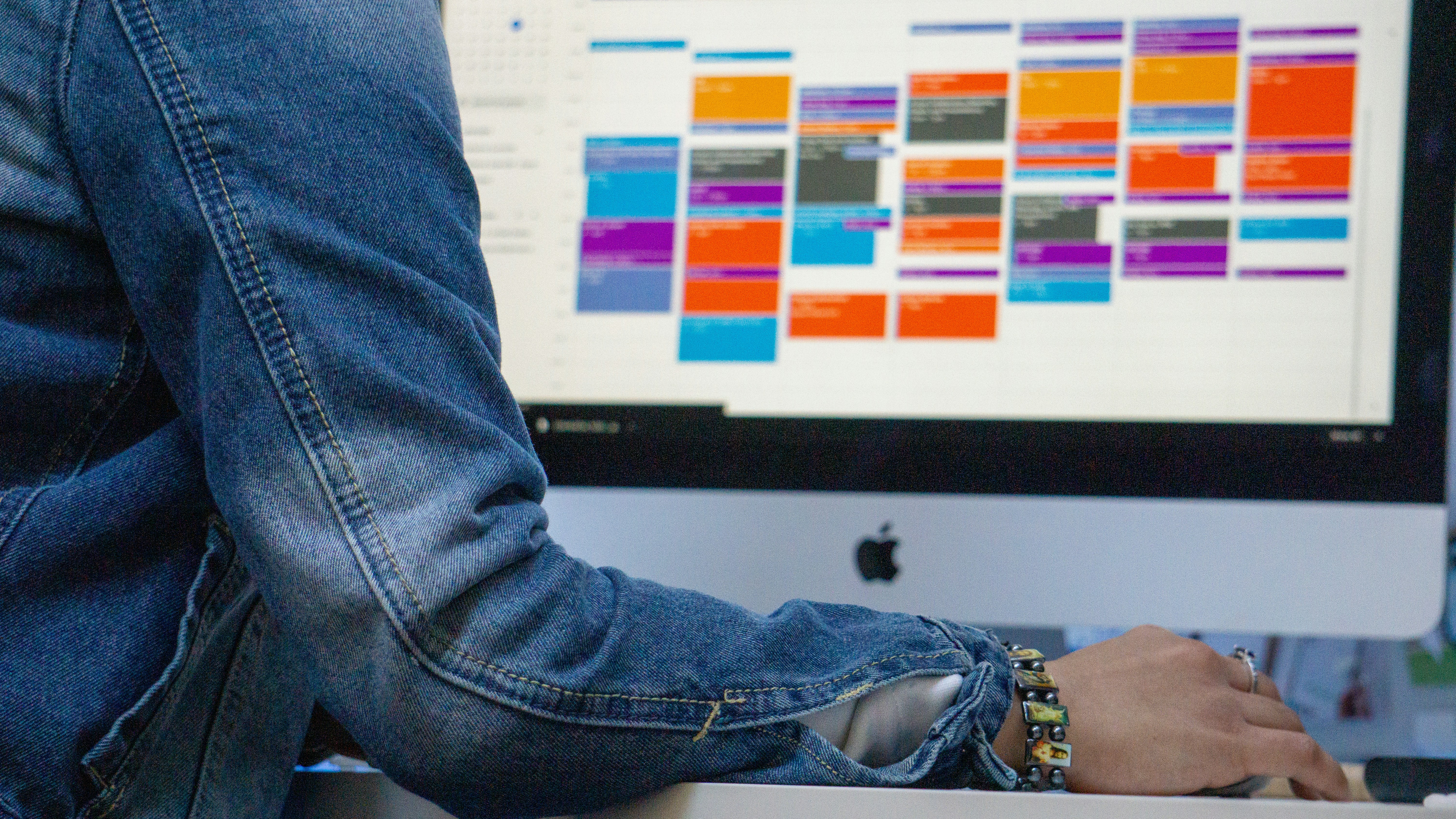 A person working at an iMac with a colorful calendar on the screen