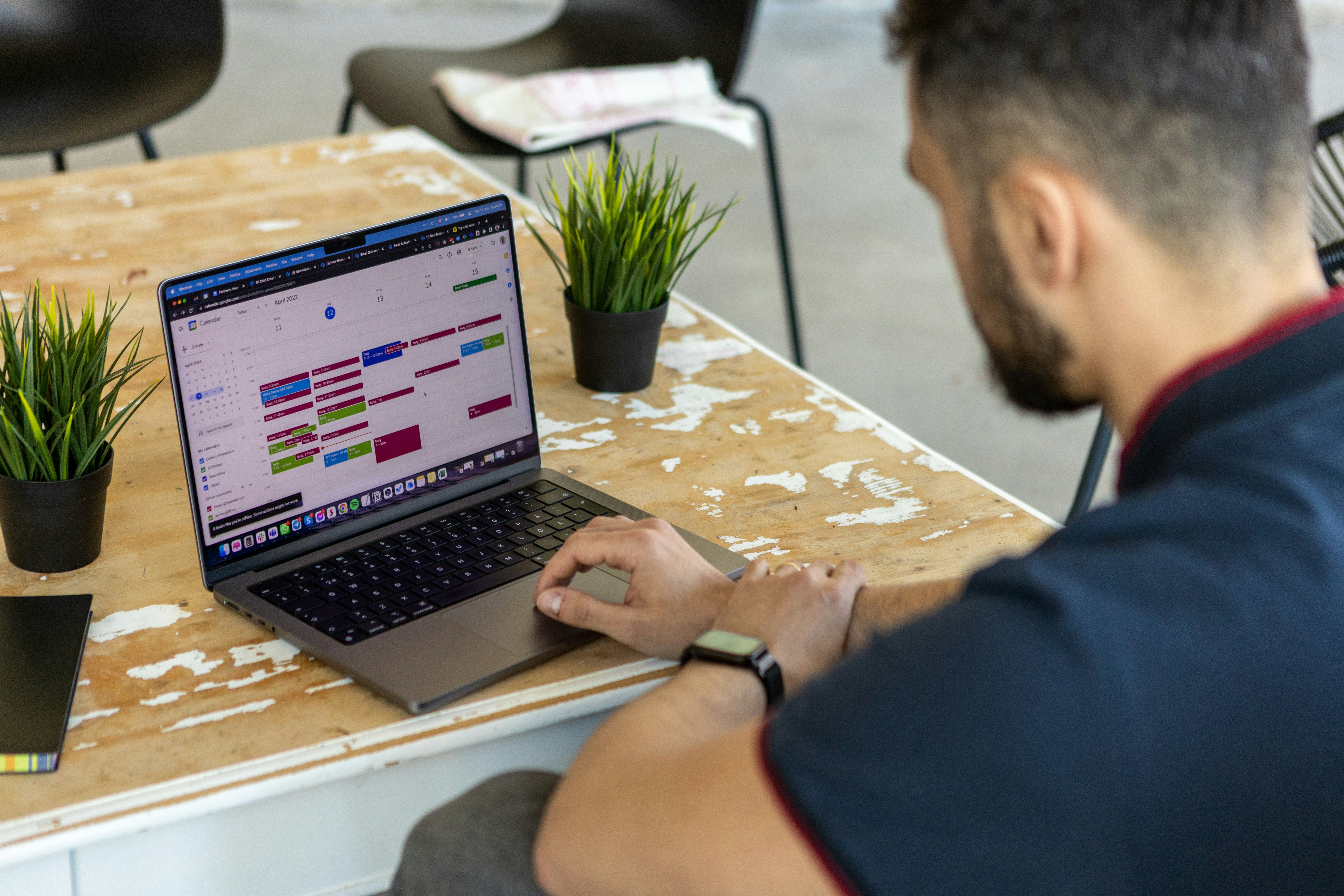A man looking at Google Calendar on a laptop at a wooden desk