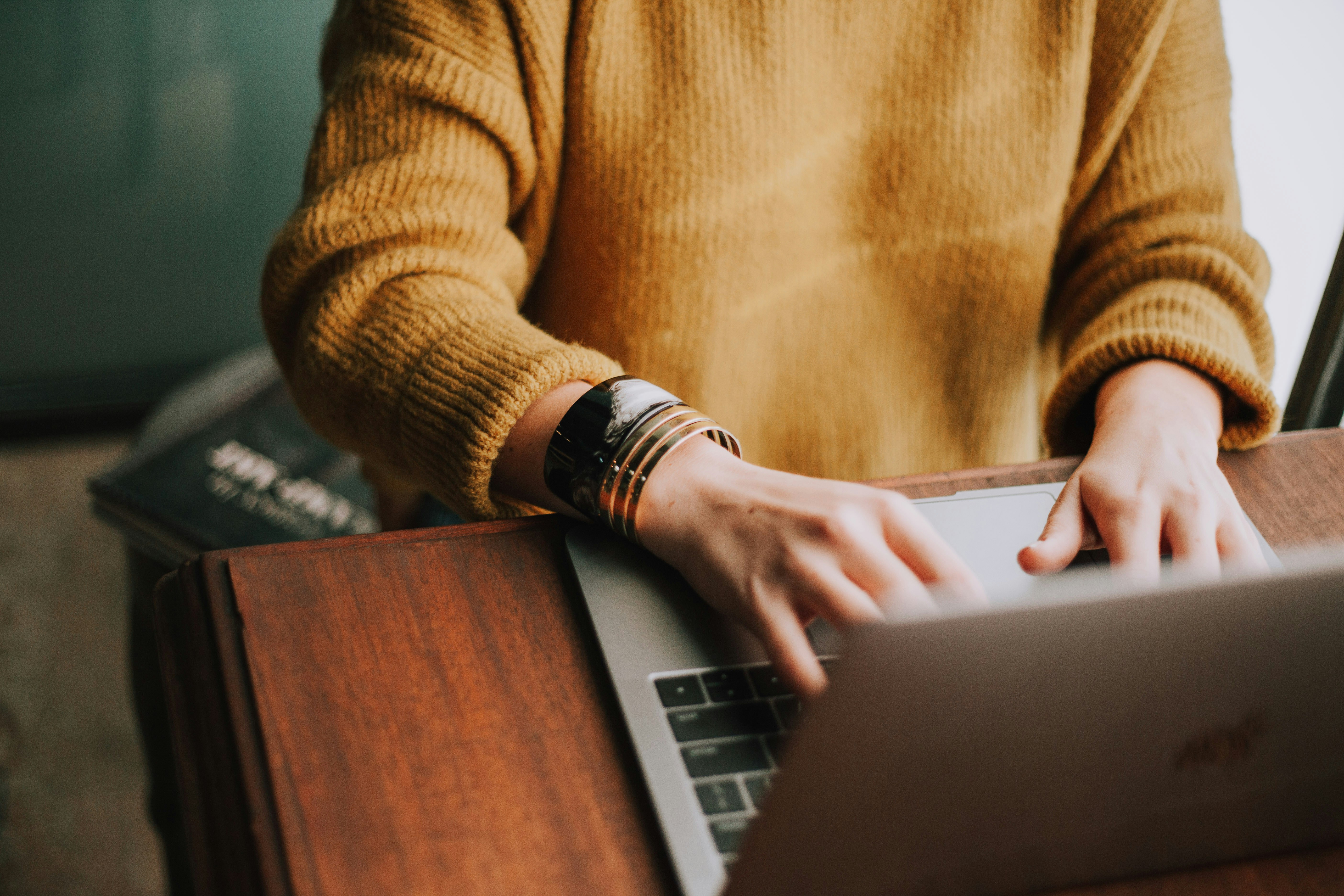A woman typing on a laptop at a wooden desk